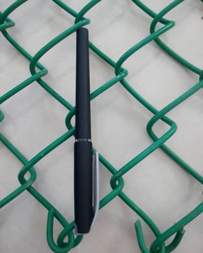 Uma pena preta é colocada no PVC verde revestiu a cerca do elo de corrente e o comprimento de dois furos é equivalente com comprimento de uma pena.